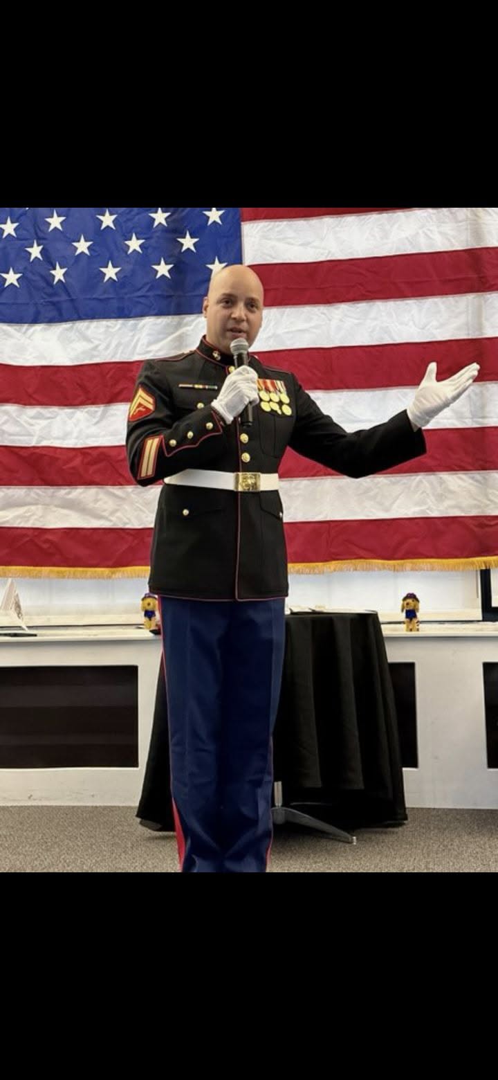 Daniel Guzman, a combat Marine veteran, speaking in his U.S. Marine Corps dress uniform in front of an American flag